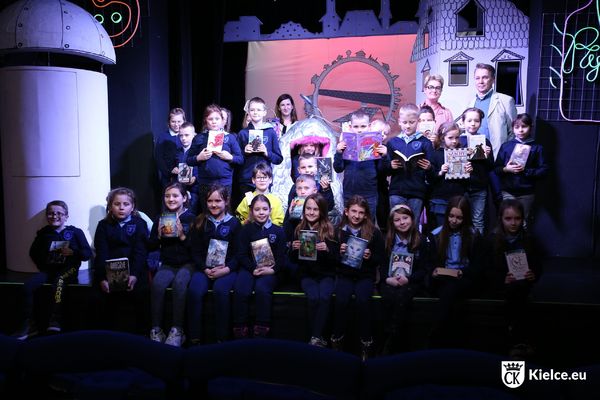 Grupa osób na scenie Teatru Lalki i Aktora Kubuś w Kielcach, dzieci trzymają książki