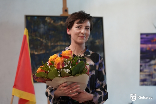 Na zdjęciu Anna Tyszewicz-Obara trzymająca kwiaty, w tle jeden z jej obrazów.