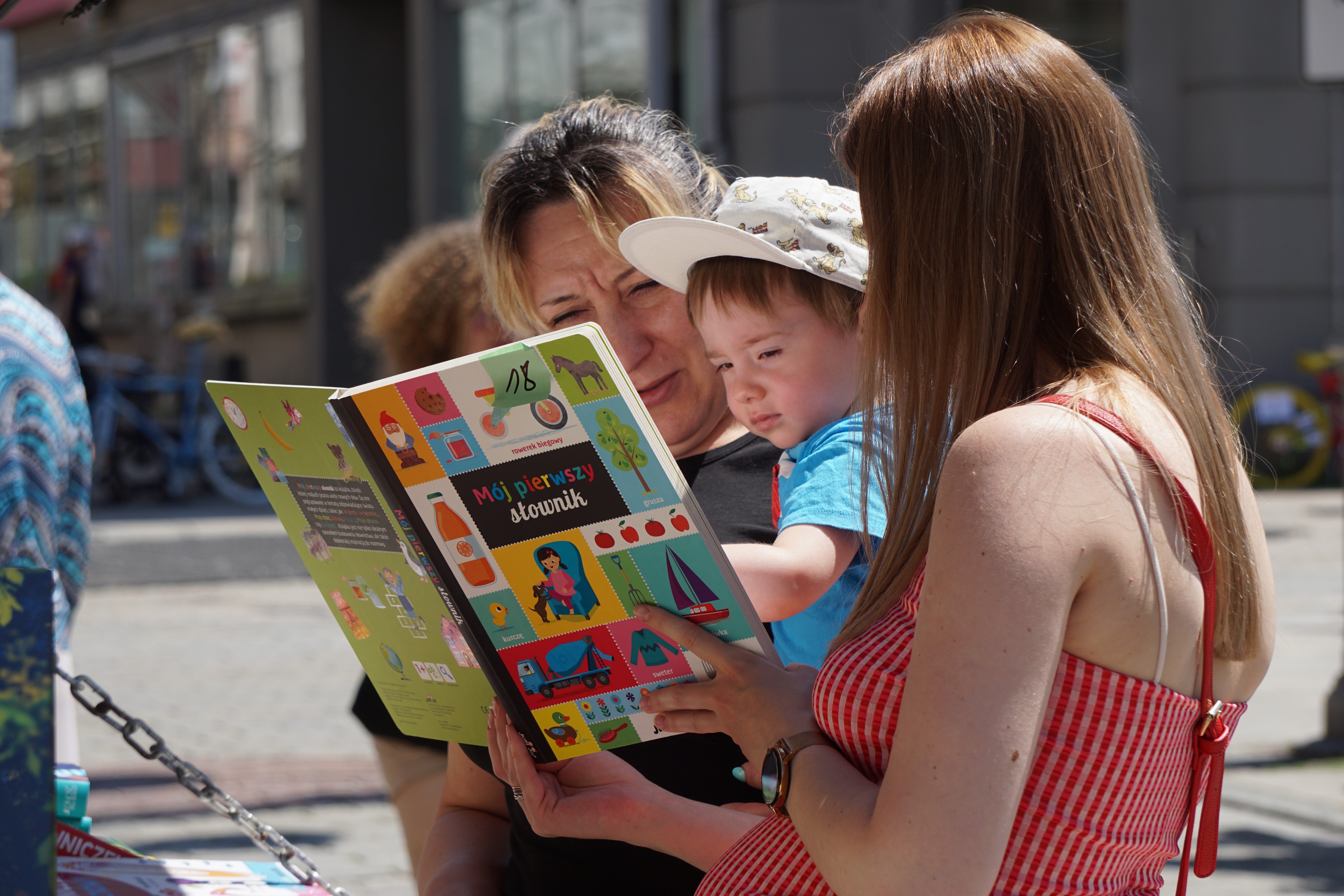 Dziecka na rękach kobiety czytające książkę. Obok stoi druga kobieta