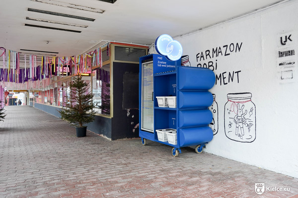 Stacja społeczna, pomalowana na niebiesko, w tle choinka i okna lokalu gastronomicznego
