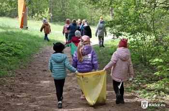 Grupa dzieci idzie przez las. Dwie dziewczynki trzymają żółty worek na śmieci.