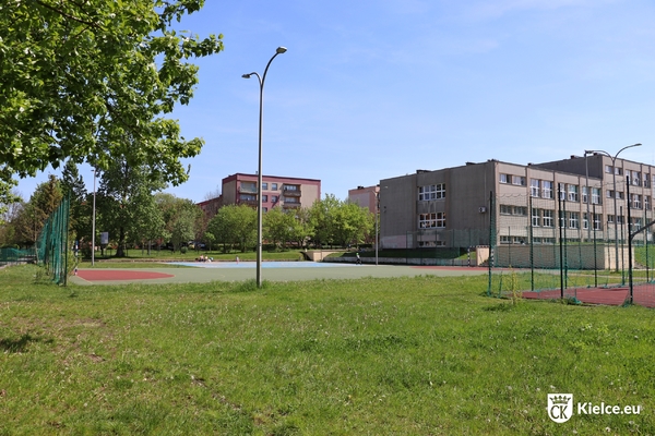 Trawnik, boiska, budynek szkoły oraz bloki mieszkalne.