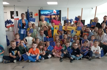 zdjęcie przedstawia grupę dzieci w punkcie promocji Kielc z flagami Unii Europejskiej