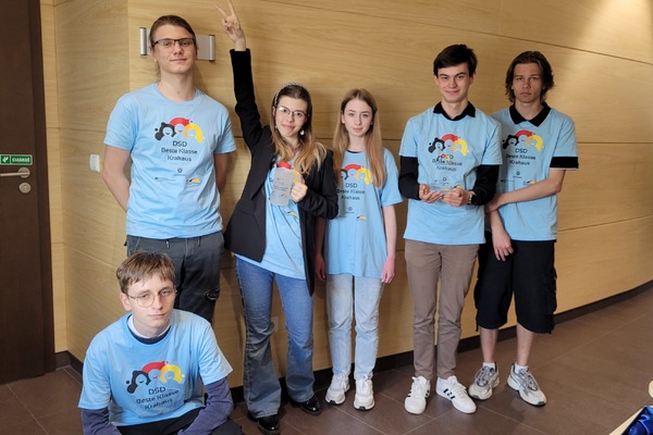 Sześcioro młodych ludzi w niebieskich koszulkach pozuje do zdjęcia. Pięć osób stoi, jedna osoba siedzi na podłodze po lewej stronie.
