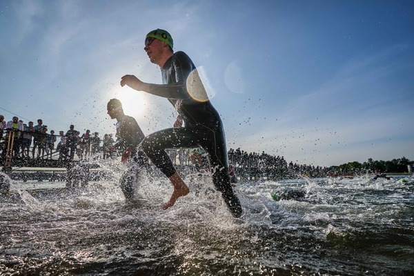 zdjęcie; triathloniści biegną brzegiem akwenu