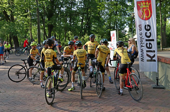 Grupa rowerzystów w żółtych koszulkach, tyłem do fotografa. 