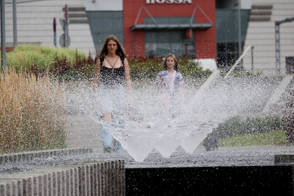 zdjęcie przedstawia dwie dziewczyny idące za fontanną, która jest na pierwszym planie