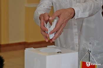 zdjęcie przedstawia wrzucanie papierowych losów do urny
