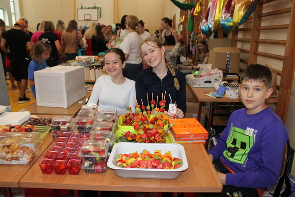 Dwie dziewczynki i chłopiec siedzą przy stoliku zastawionym przekąskami z owoców