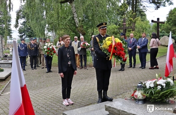 Prezydentka Agata Wojda, po prawej stronie strażnik miejski trzyma wieniec. Na drugim planie stoi kilkanaście osób.