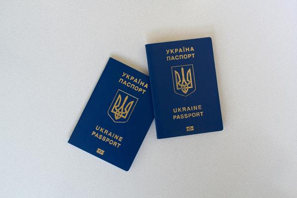 Dwie granatowe książeczki paszportowe ze złotymi napisami w języku ukraińskim.