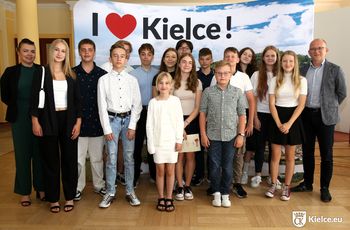 Grupa dzieci, młodzieży i osób dorosłych pozuje do zdjęcia. W tle ścianka z napisem I love Kielce.