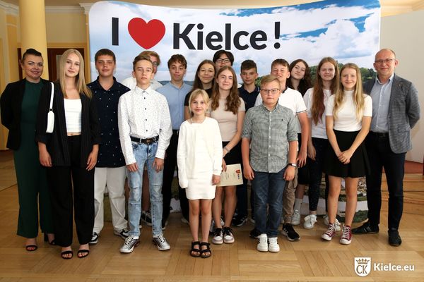 Grupa dzieci, młodzieży i osób dorosłych pozuje do zdjęcia. W tle ścianka z napisem I love Kielce.