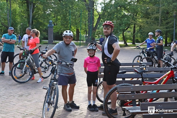Straszy mężczyzna i młody mężczyzna oraz mała dziewczynka w kaskach rowerowych stoją obok swoich rowerów.