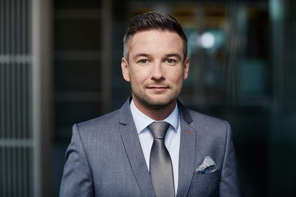 Zdjęcie portretowe. Paweł Kułaga w jasnobłękitnej koszuli oraz szarej marynarce i szarym krawacie.