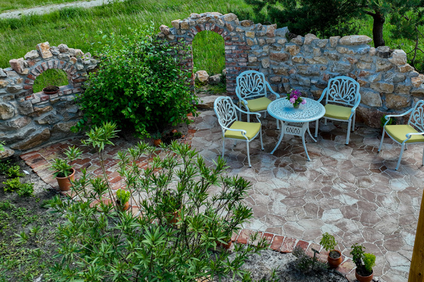 Kącik śródziemnomorski w Ogrodzie Botanicznym, stolik, trzy krzesełka, ozdobny murek, rośliny