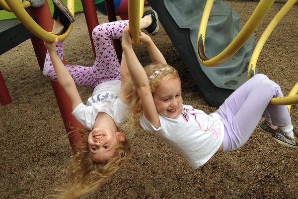 Dwie dziewczynki ubrane w białe bluzki i fioletowe getry bawią się na placu zabaw.