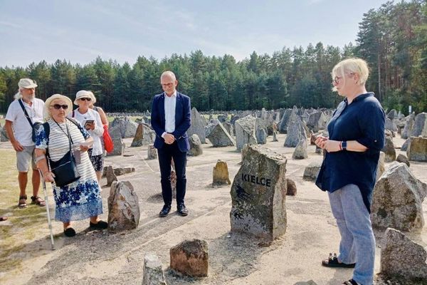 Pięć osób stoi przy kamieniu upamiętniającym ofiary zagłady