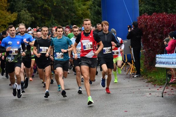 Kilkadziesiąt osób w strojach sportowych biegnie po trasie, po prawej stronie stolik z wodą, fotograf i dwoje dzieci