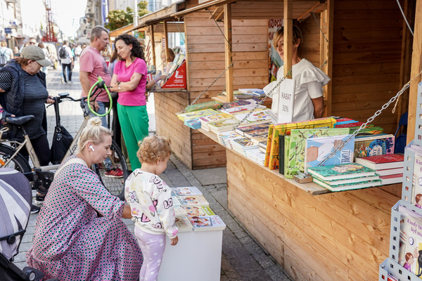 Stoiska z książkami na ul. Sienkiewicza, kobieta z małą dziewczynką oglądają książki, na drugim planie dwie kobiety i mężczyzna