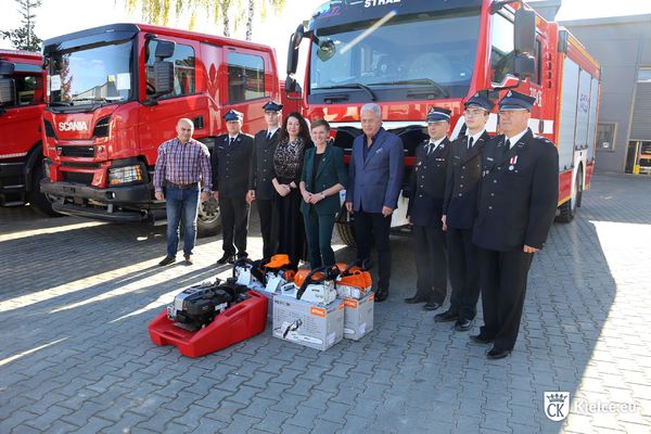 Kilka osób pozuje do zdjęcia na tle wozu strażackiego