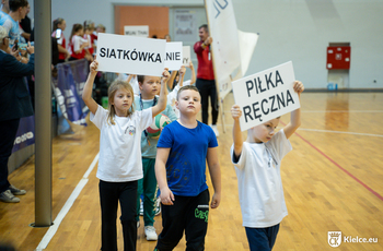 Kilkoro dzieci, dwoje trzyma kartony z napisami piłka ręczna oraz siatkówka