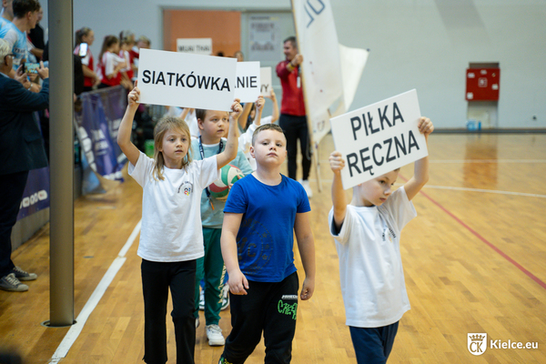 Kilkoro dzieci, dwoje trzyma kartony z napisami piłka ręczna oraz siatkówka