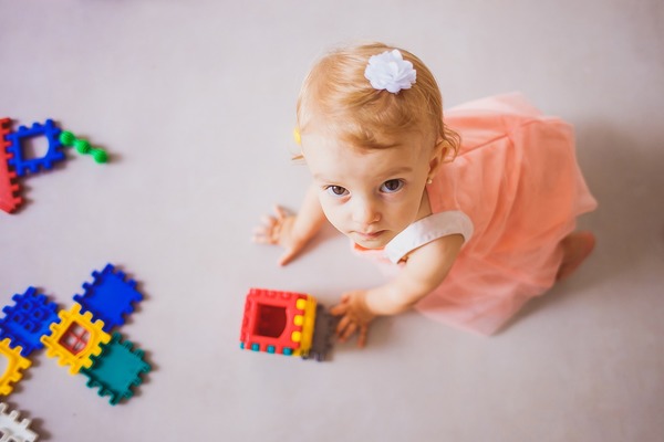 Mała dziewczynka w łososiowej sukience bawi się kolorowymi klockami.